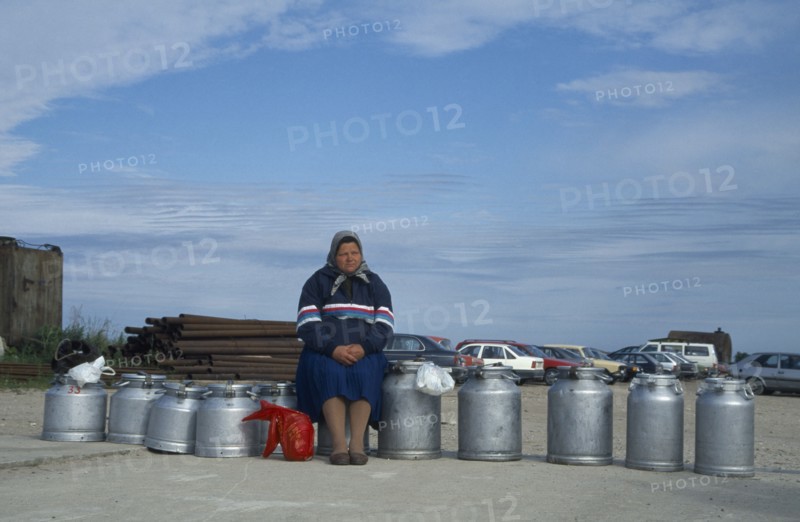 ESTONIA, Baltic Coast, Woman sitting on milk cans waiting for ferry.