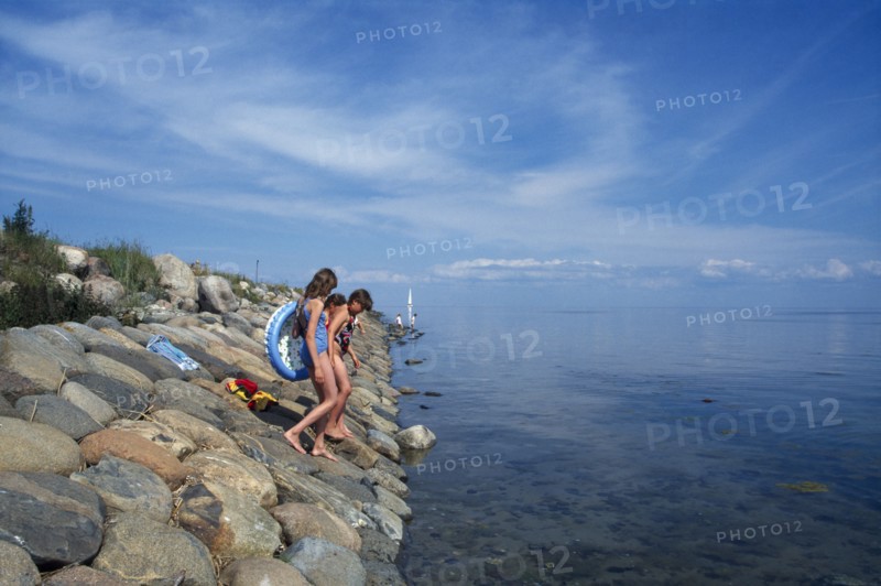 ESTONIA, Kihnu Island, Group of young girls wlking down stone sea defence into water off the Baltic coast.