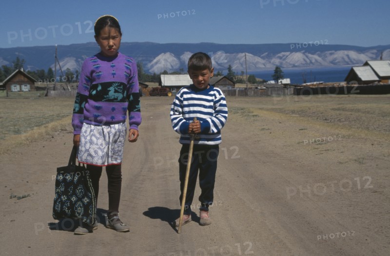 RUSSIA, Siberia, Lake Baikal, Buryat children with farmstead and lake behind.  The Buryat are of Mongolian descent and are the largest ethnic minority group in Siberia.