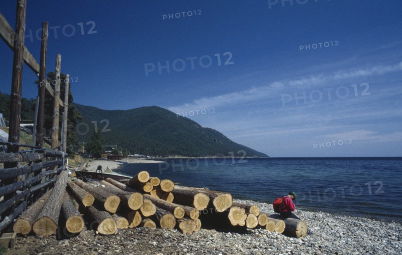 RUSSIA, Siberia, Lake Baikal, Person sitting on length of cut timber on lake shore.