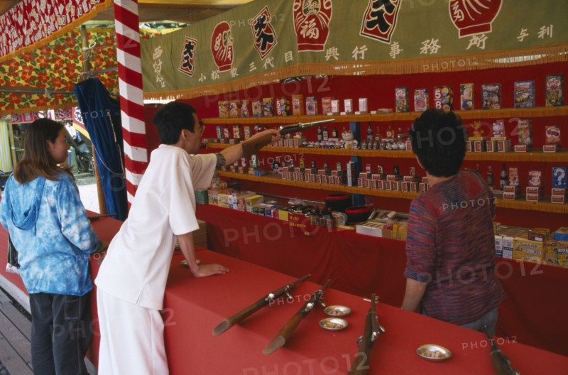 JAPAN, Honshu, Chiba, Narita.  Young couple at shooting range pointing out prizes available to win.