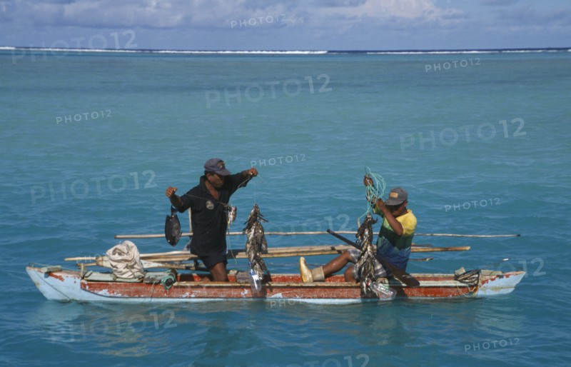 PACIFIC ISLANDS, Polynesia, Cook Islands, Aitutaki Lagoon.  Fishermen in wooden canoe pulling up fishing lines and catch.
