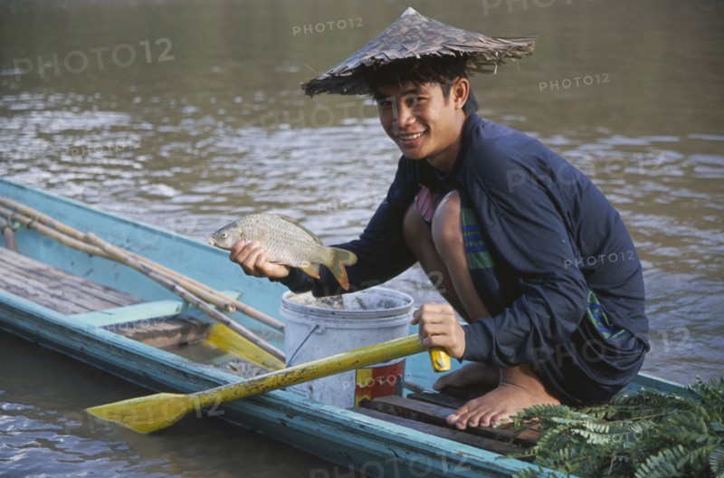 LAOS, Luang Prabang, Fisherman  crouched on wooden canoe on the Mekong River holding up fish.
