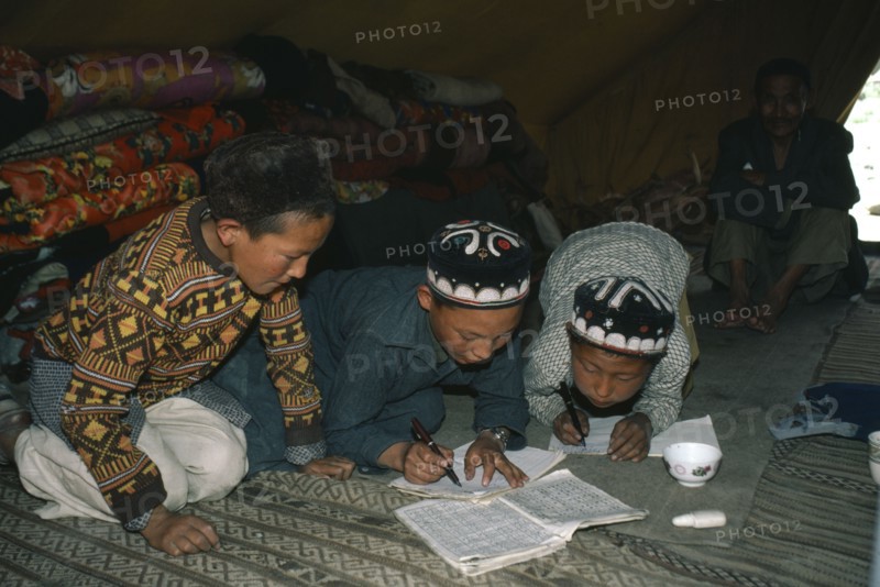 AFGHANISTAN, Tribal People, Kirghiz children writing inside yurt with man sitting beside doorway behind.