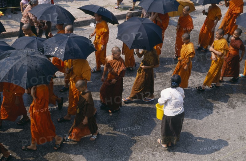 LAOS, Luang Prabang, Line of monks holding umbrellas to protect themselves with water being thrown during New Year celebrations.