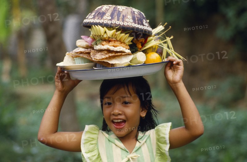 INDONESIA, Bali, Laughing Balinese girl carrying food offerings on her head.