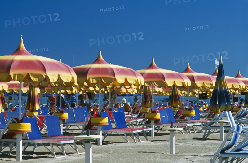 ITALY, Emilia-Romagna, Rimini, "Lines of red, yellow and blue parasols and sun loungers on sandy beach."