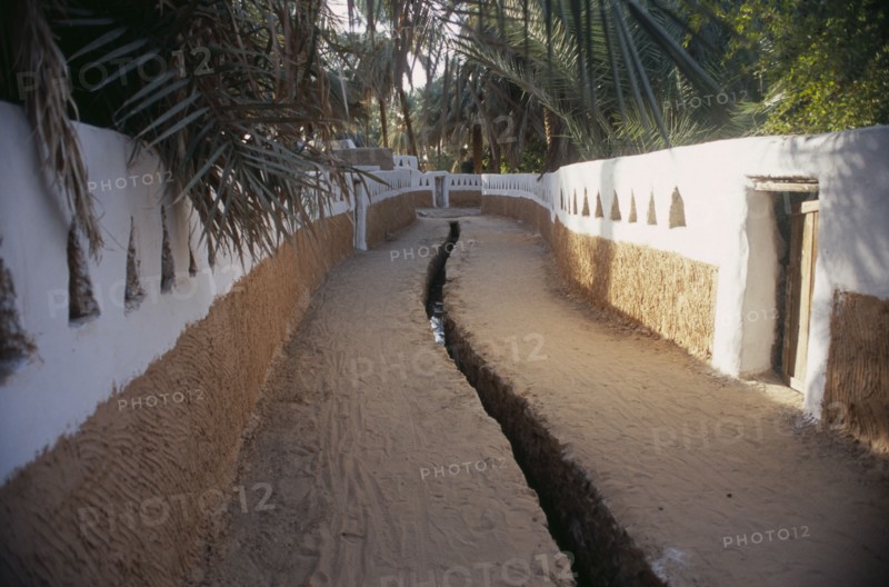 LIBYA, Ghadames, Deep irrigation channel through street between walls partly painted white with triangular cut outs.