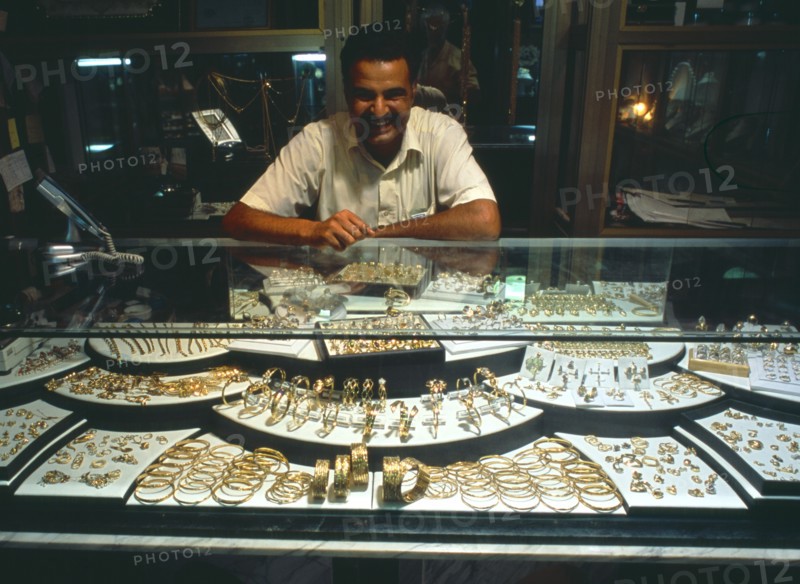 LIBYA, Zawia, Jeweller behind display of gold items in glass topped cabinet.
