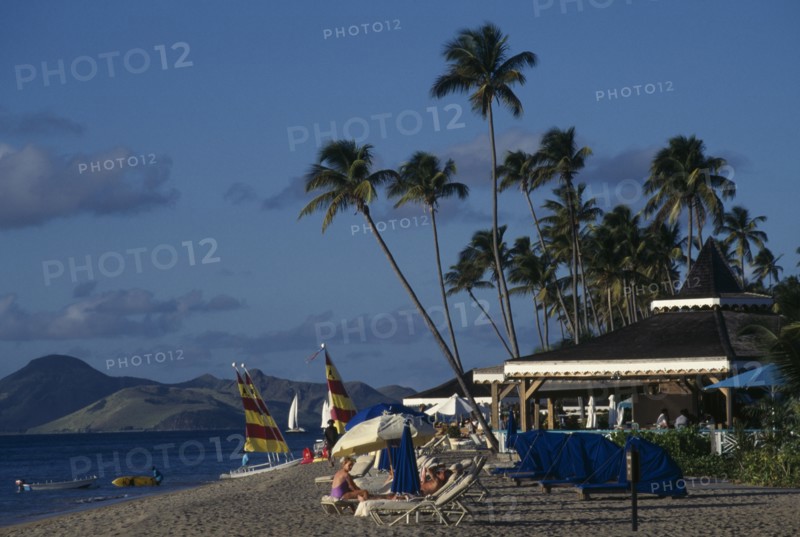 WEST INDIES, Nevis, View along beach with sails and sunbeds beside beach bars of the Four Seasons Hotel