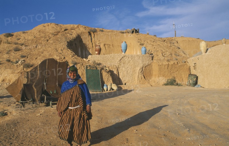 TUNISIA, Zaraova, Portrait of a Berber woman standing outside her home which is dug out of a hillside