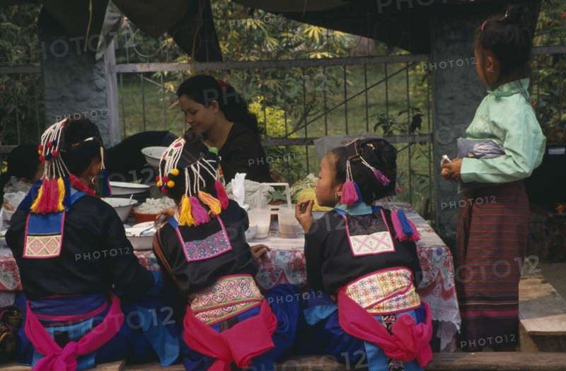 LAOS, Luang Prabang, Hmong girls in traditional dress eating at roadside foodstall.