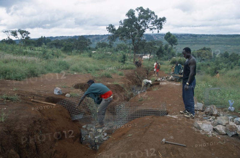 TANZANIA, West, Great Lakes Region, Refugees making gambions to prevent water erosion.  Base of structure is stone filled wire cages covered with earth.