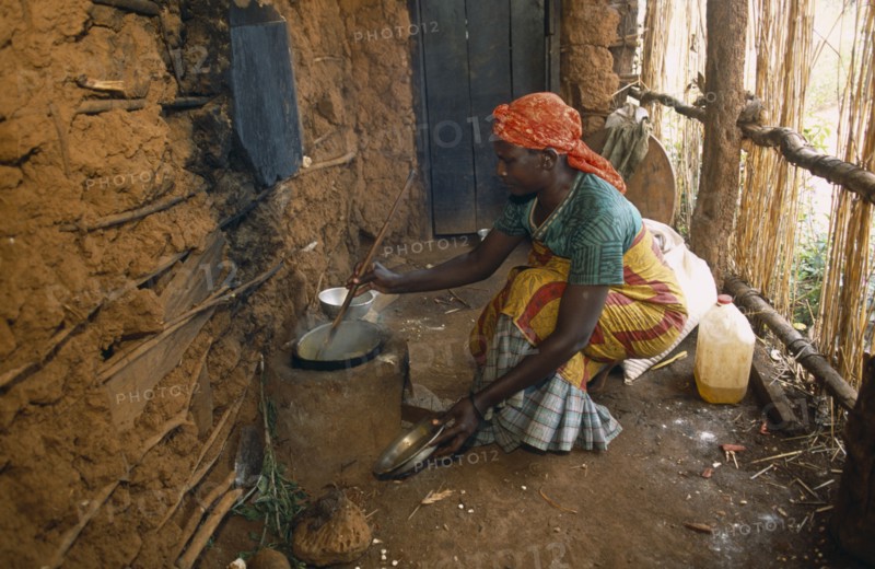 TANZANIA, West, Great Lakes Region, Refugee woman cooking on wood saving clay stove inside hut with mud brick walls.