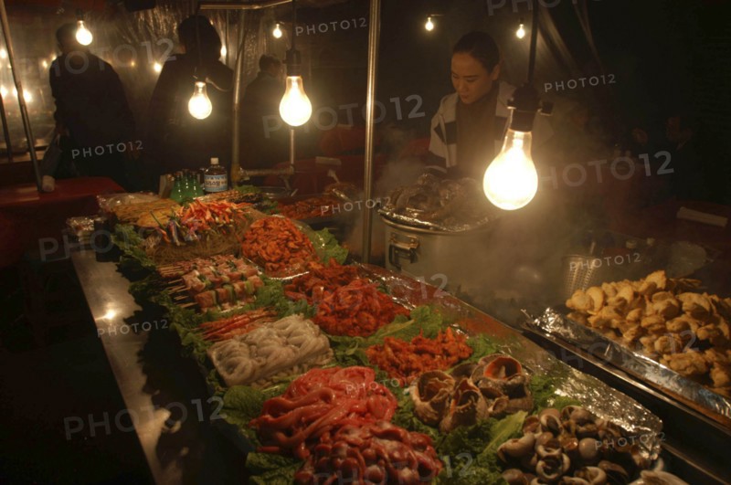 KOREA, Seoul, "Namdaemun Market on a cold December night with a woman cooking behind trays of fresh seafood, pork, chicken and beef with plastic sheeting to keep out cold"