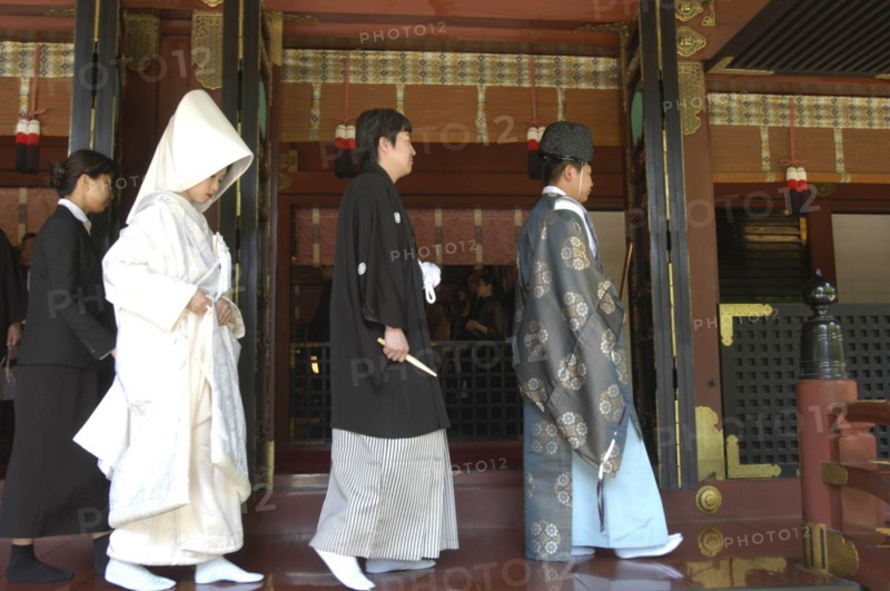 JAPAN, Honshu, Tokyo, Nezu. Shinto priest leads newly married couple out of Nezu Jinja shrine after Shinto ceremony with bride and groom in traditional costume