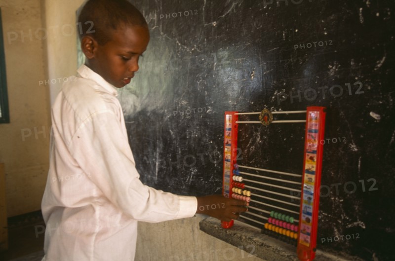 SOMALILAND, Hargeisa, Boy using an abacus in school classroom with blackboard on wall behind.