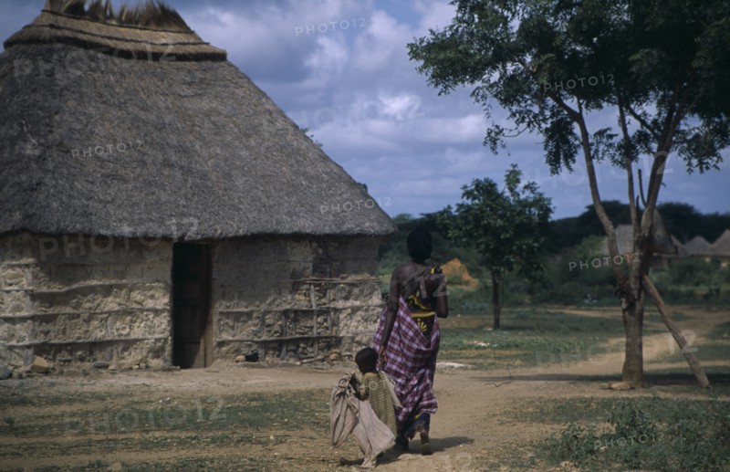 SOMALIA, Tribal People, Woman and child walking towards traditional thatchedhouse near Baidoa.