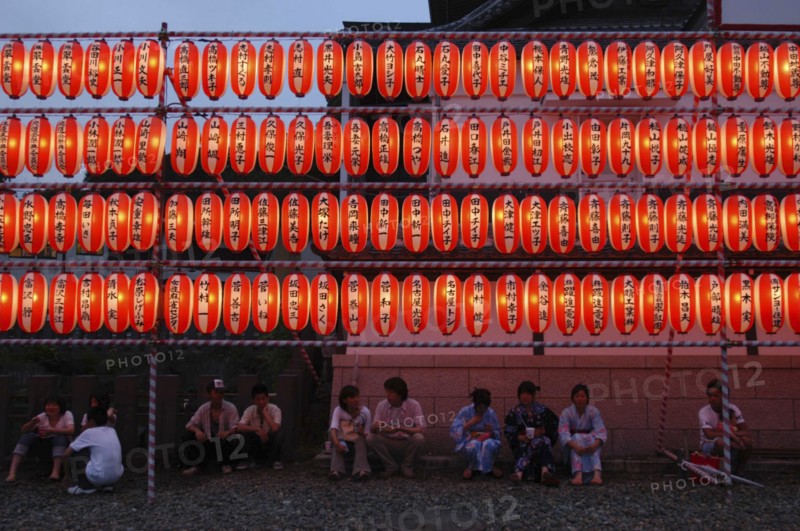 JAPAN, Chiba, Narita, Festival goers at the Gion Matsuri rest under rows of illuminated chochin lanterns with name of donor to Narita san Temple written on each