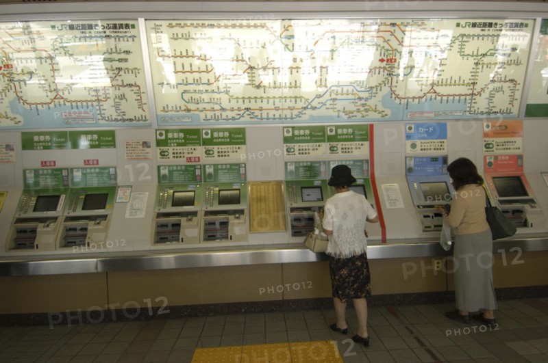 JAPAN, Honshu, Tokyo, Ueno train station with women buying train tickets from vending machines with the train route map above