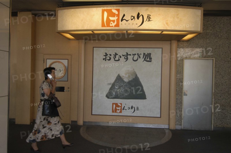 JAPAN, Honshu, Tokyo, Onigiri rice ball shop sign in front of Tokyo Station with passing woman using cell phone