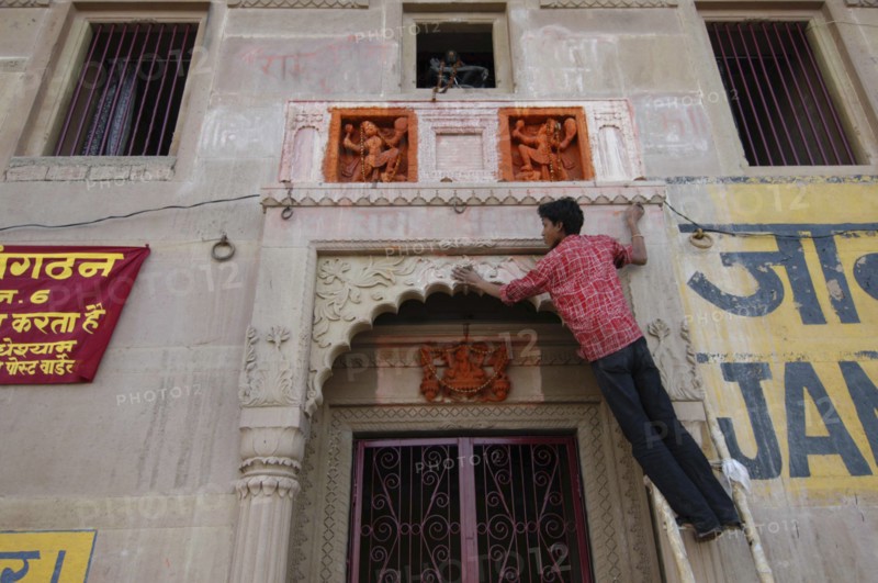 INDIA, Uttar Pradesh, Varanasi , Deep Diwali Festival with young man decorating a doorway