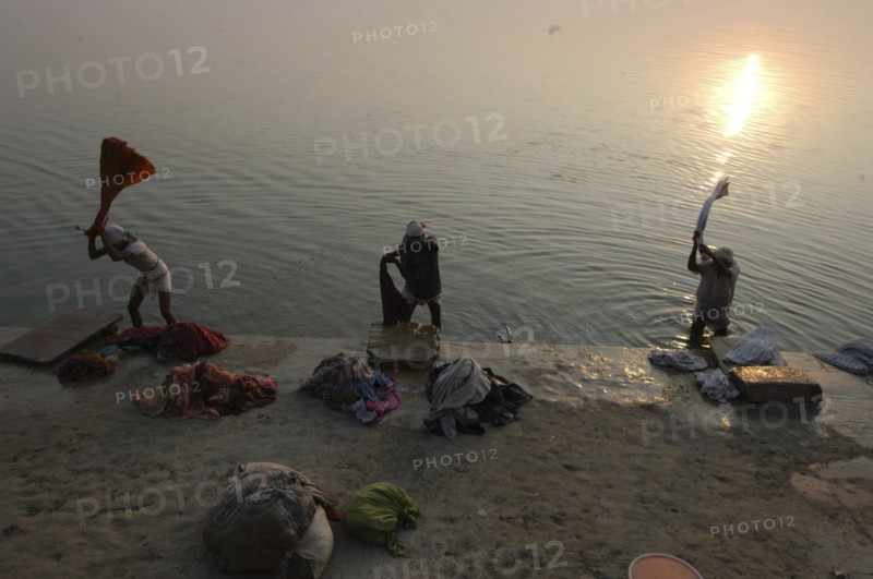 INDIA, Uttar Pradesh, Varanasi , Near Shivala Ghat. Dhobi clothes washers working on the banks of the Ganges River with low sun on the horizon