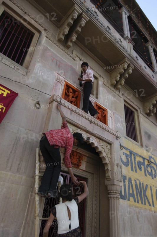 INDIA, Uttar Pradesh, Varanasi , Deep Diwali Festival with teenage boys climbing a doorway to decorate Hindu shrine