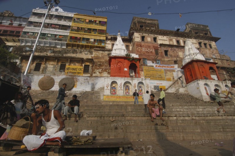 INDIA, Uttar Pradesh, Varanasi, Dasashwamedh Ghat. View looking up at a temple and the houses behind the ghats with a Hindu Bhramin pundit sitting waiting for his next customer on the steps