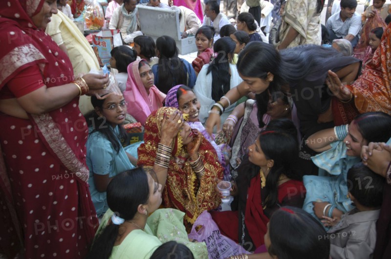 INDIA, Uttar Pradesh, Varanasi, Sankat Mochan Mandir temple. Women friends and relatives cheer a bride with her head draped in a red sari at her wedding outside the temple