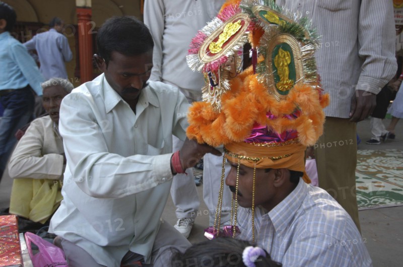 INDIA, Uttar Pradesh, Varanasi, Sankat Mochan Mandir temple. A groom having his headdress / hat adjusted at his wedding outside the temple