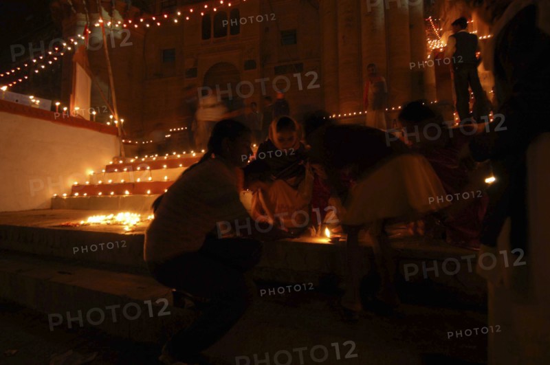INDIA, Uttar Pradesh, Varanasi, Deep Diwali Festival with young girls lighting oil lamps on steps leading down to the Ganges River