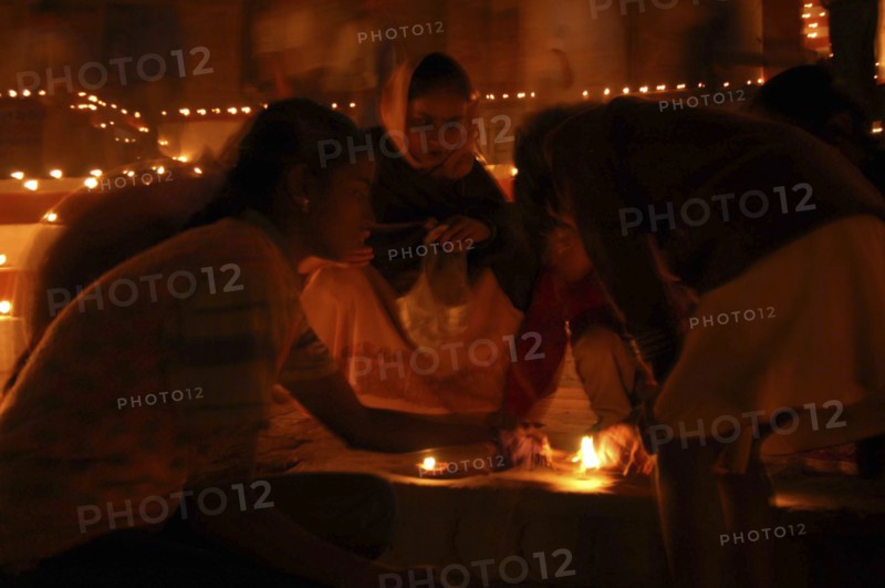 INDIA, Uttar Pradesh, Varanasi, Deep Diwali Festival with young girls lighting oil lamps on steps leading down to the Ganges River