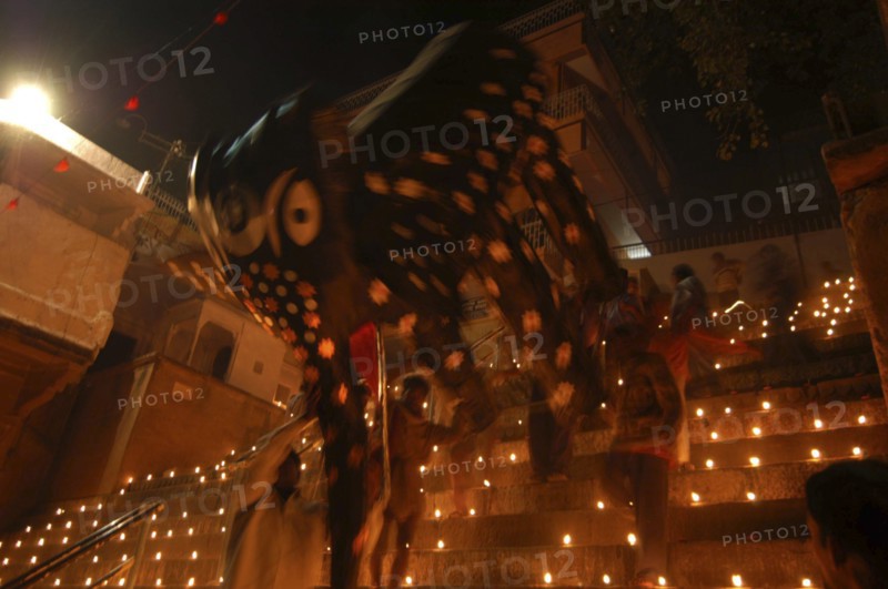 INDIA, Uttar Pradesh, Varanasi, Deep Diwali Festival. Men carry a paper statue of the Hindu God Ganesh down steps covered in oil lamps leading to the Ganges River