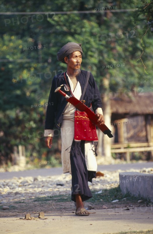 MYANMAR, Kachin State, Myitkyina, Manou grounds. Old Jinghpaw man in traditional attire with sword and shoulder bag