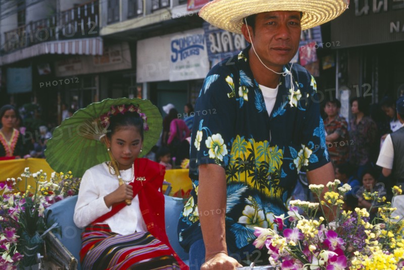 THAILAND, Chinag Mai, Young girl riding rickshaw driven by man in the Flower Festival Parade