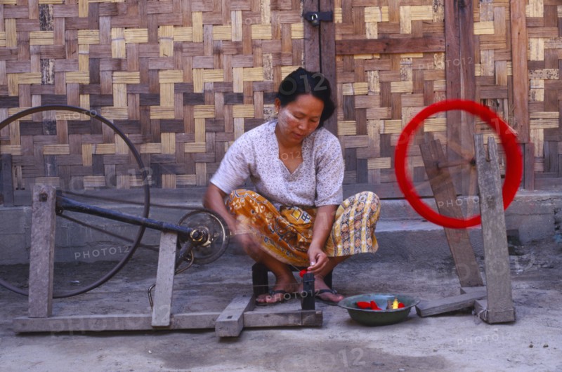 MYANMAR, Kachin State, Myitkyina, Jinghpaw woman spinning thread onto a bobbin for weaving at a weavers shop