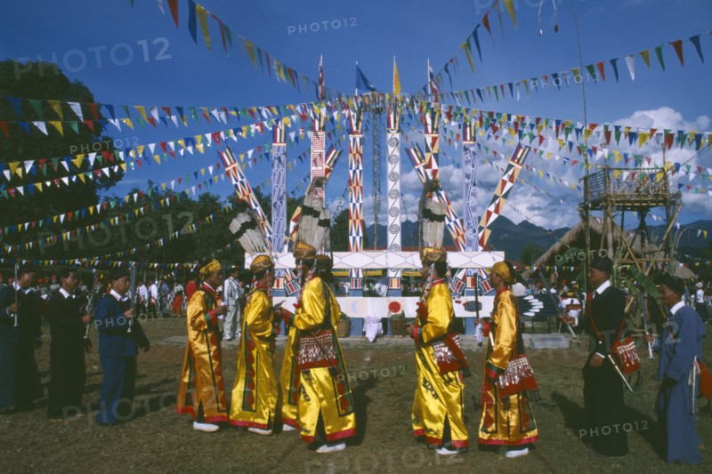 THAILAND, Chiang Mai, Samathi Mai, Kachin Manou Dance leaders passing Manou posts in the background
