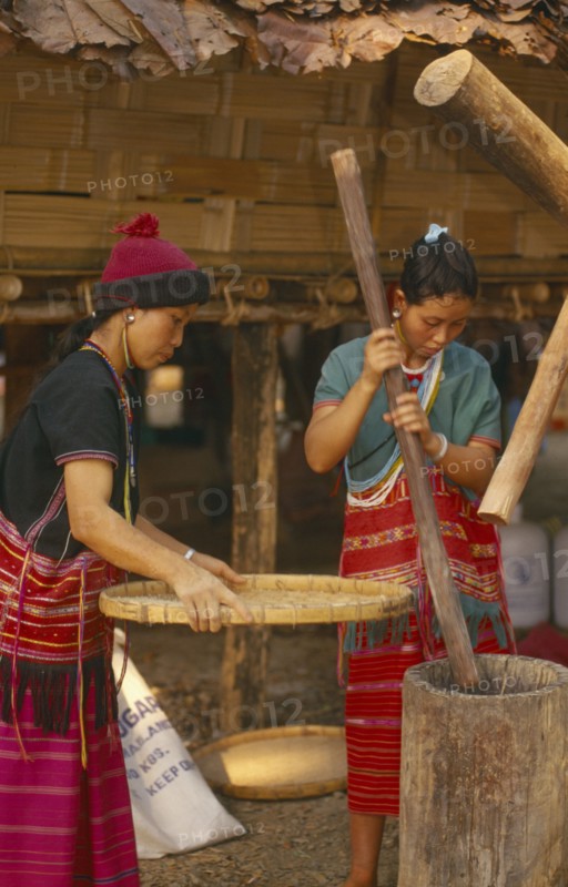 THAILAND, Chiang Mai, Sgaw Karen woman pounding rice by hand while another sifts with a large bamboo tray