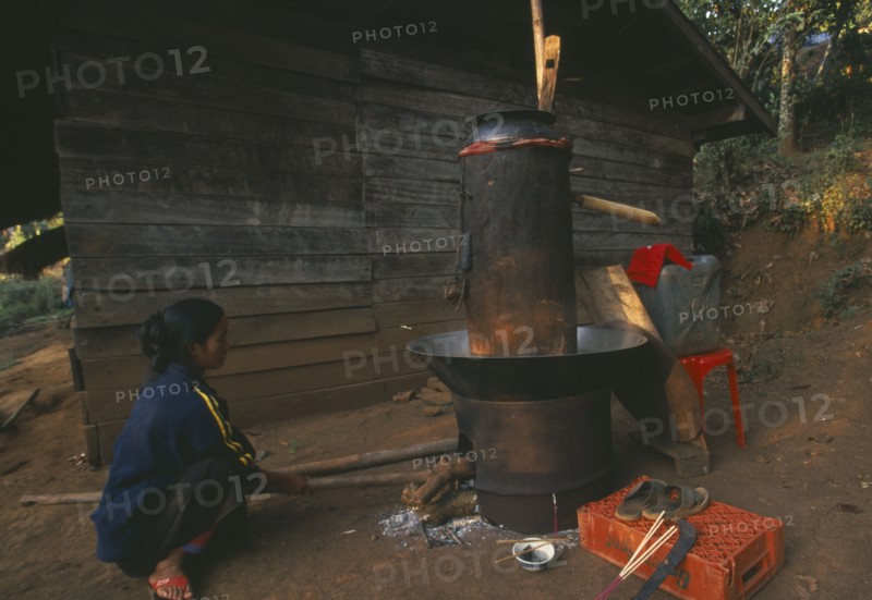 THAILAND, Chiang Rai Province, Doi Lan, Lisu woman stoking fire of her still for making corn whiskey