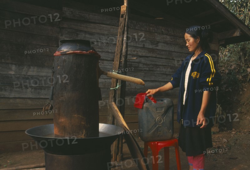 THAILAND, Chiang Rai Province, Doi Lan, Lisu woman checking cloth filter on the spout of her still for making corn whiskey