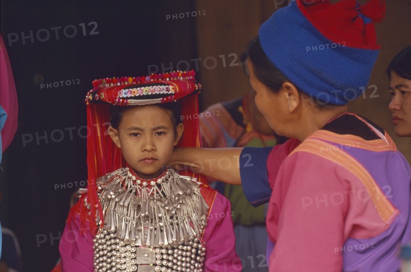 THAILAND, Chiang Rai Province, Huai Khrai, Young Lisu girl dressed in her New Year finery while her mother adjusts her silver neck chain