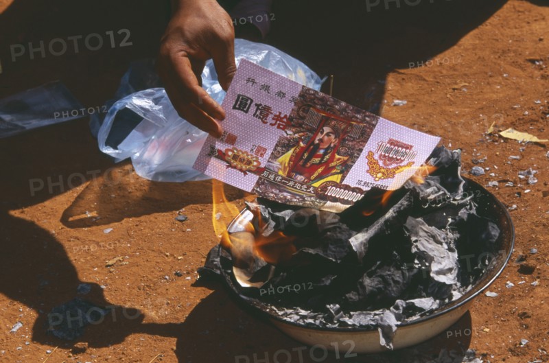 THAILAND, Chiang Mai Province, Bahn Mae Phaem, Lisu man burning imitation paper money for New Year