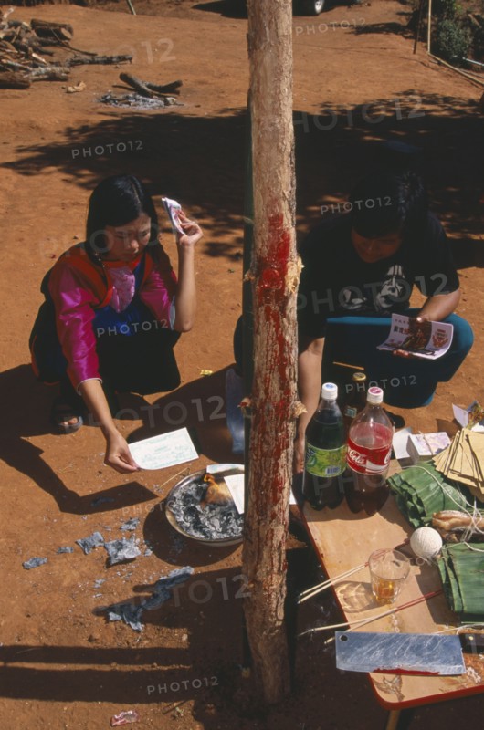 THAILAND, Chiang Mai Province, Bahn Mae Phaem, Lisu girl and man burning imitation money beside New Year tree with chicken blood on the trunk