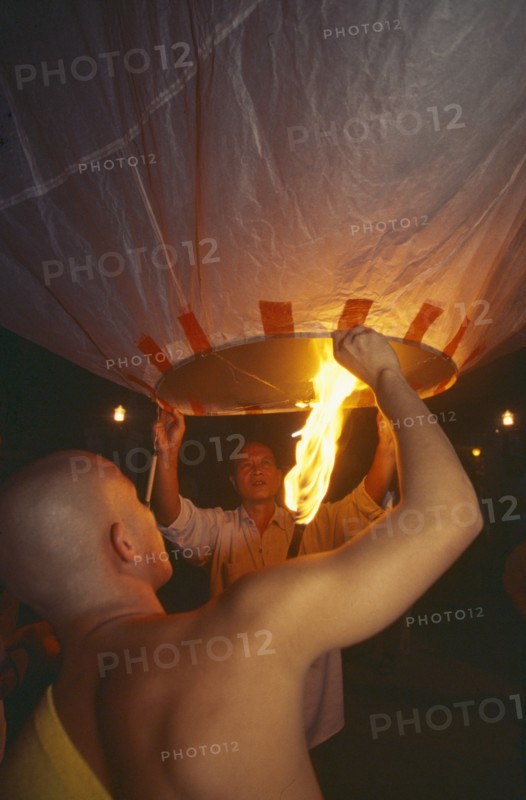 THAILAND, Chiang Mai, Mae Jo San Sai District, Loi Krathong Festival aka Yi Peng. Monk and another man launching hot air balloon into the night sky