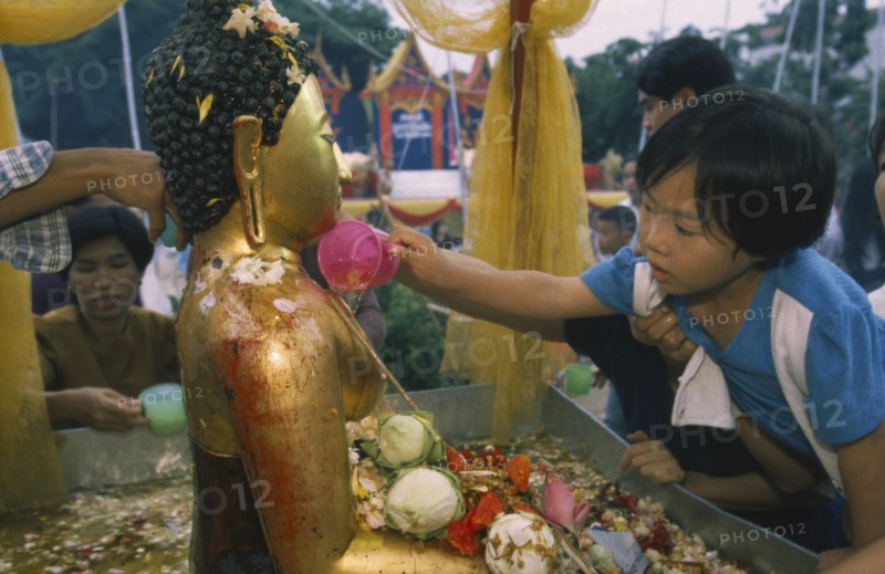 THAILAND, Chiang Mai, Wat Jedi Luang, Inthakhin Ceremony. Young boy bathing Phra Fon Saen Ha Buddha statue surrounded by floral offerings and pool