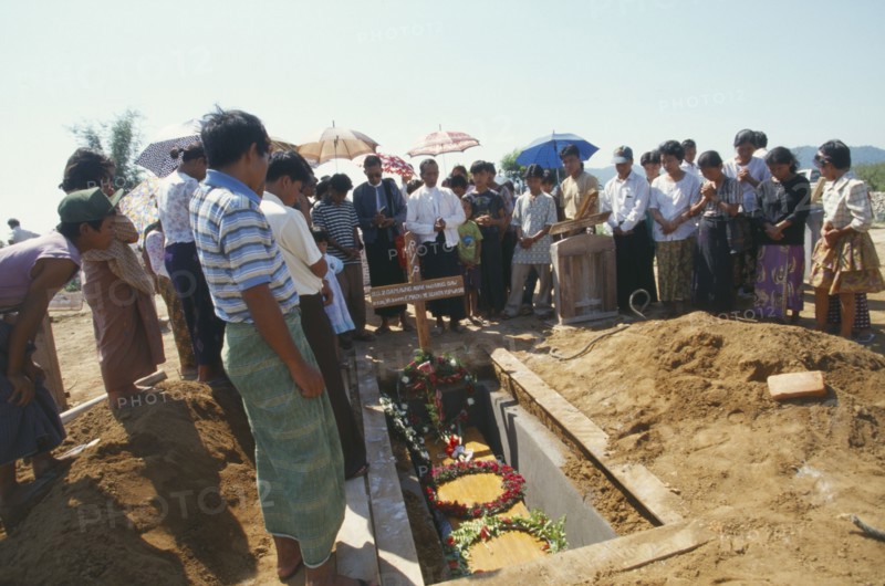 MYANMAR, Kachin State, Myitkyina, Jinghpaw Baptist funeral service with family gathered around grave near Prayer Mountain