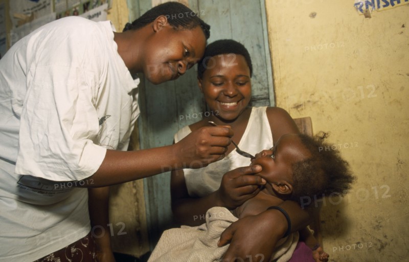 UGANDA, General, Young child held by mother receiving medicine on spoon.