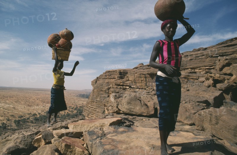 MALI, Bandiagara Cliffs, One woman carrying beer and another pots on their heads standing at the top of the Bandiagara Escarpment on their way to village market.