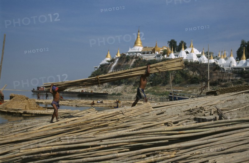 MYANMAR, Mandalay, Unloading lengths of cane on the banks of the Ayeyarawady overlooked by temple behind.
